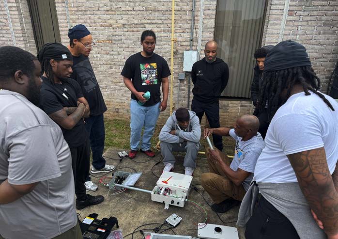 A group of students receive hands-on solar installation instruction outside.