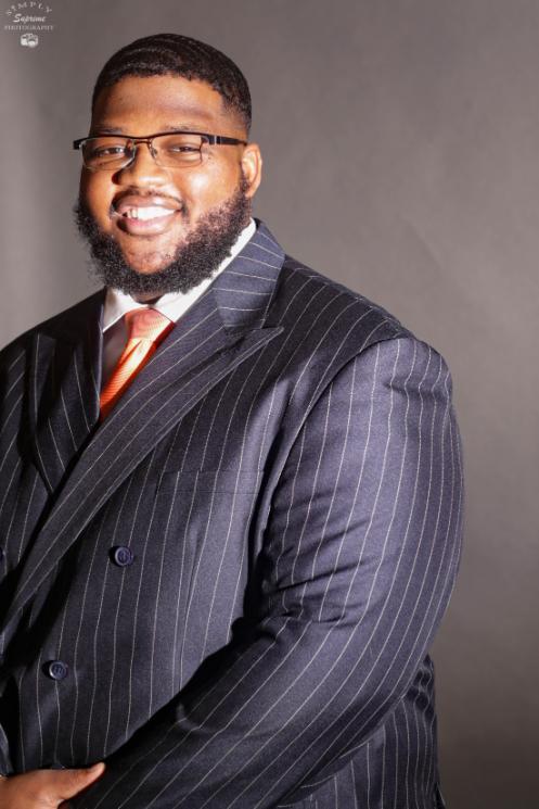 PGCC alum Marques Carr smiles in a dark blue pinstripe suit and a red tie.