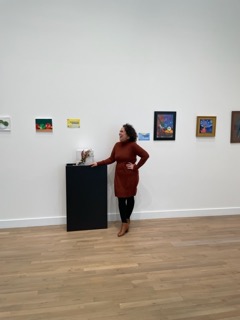 Samantha Howard smiles in a burgundy dress standing next to her gift-wrapping exhibition at PGCC's Center for Performing Arts building.