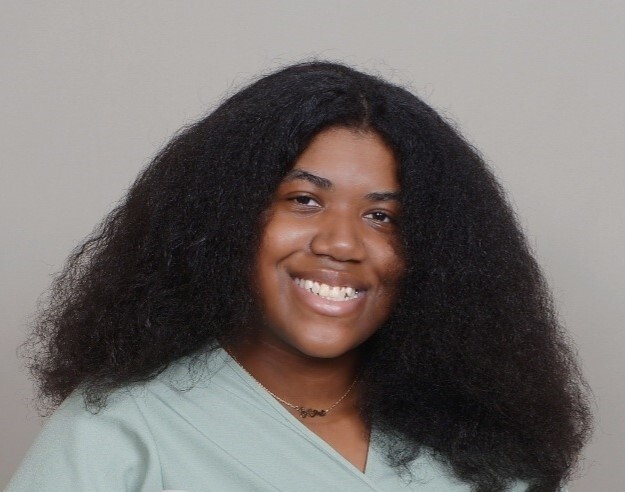 Sage Despeignes, 21, smiles in a portrait image against a gray background.