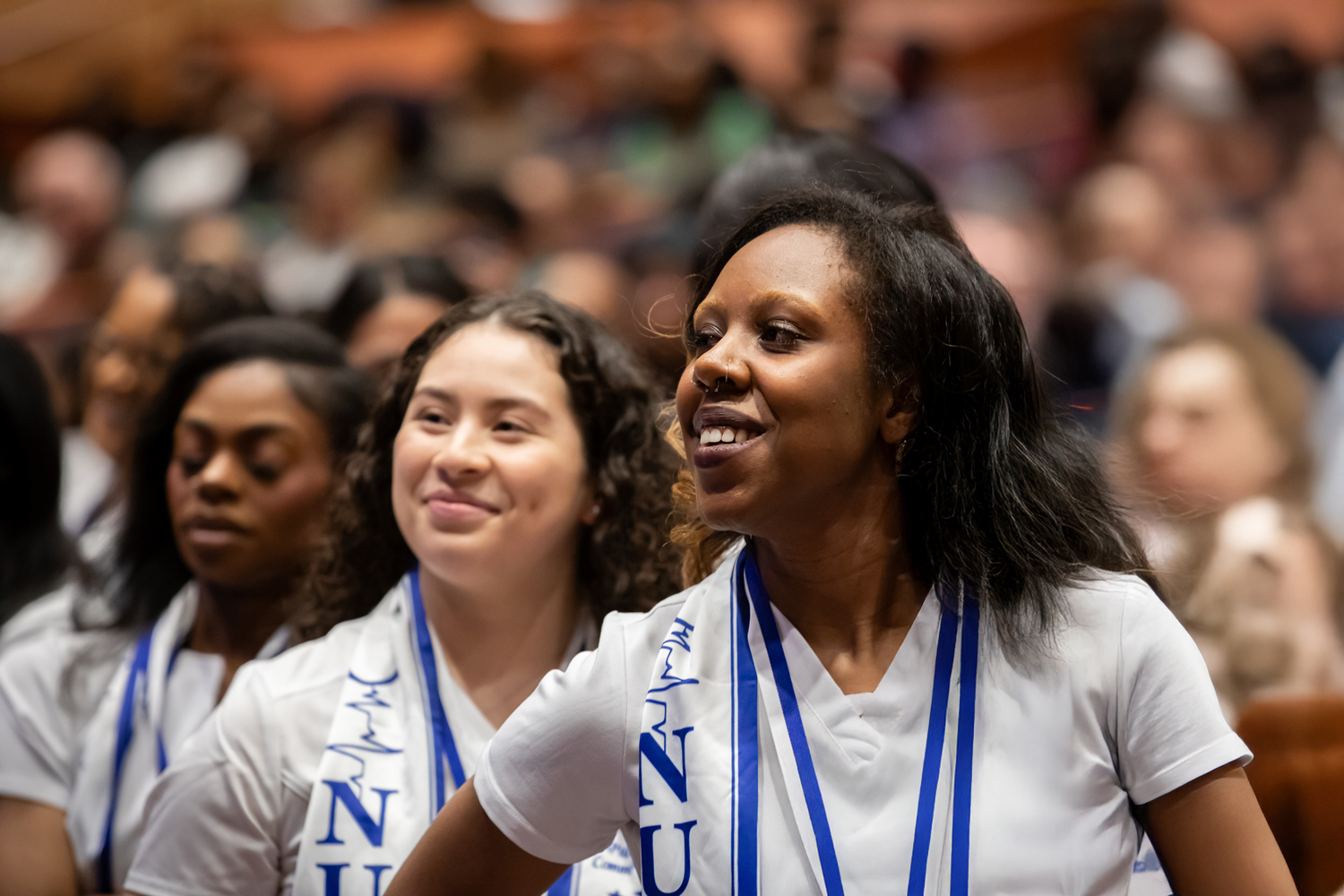 Nursing students wearing white uniforms and blue stoles smiling during a pinning ceremony