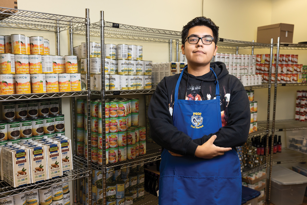 Kevin Martinez volunteers in the College’s Owl Market to ensure food access for all students. Martinez is standing in front of canned goods.