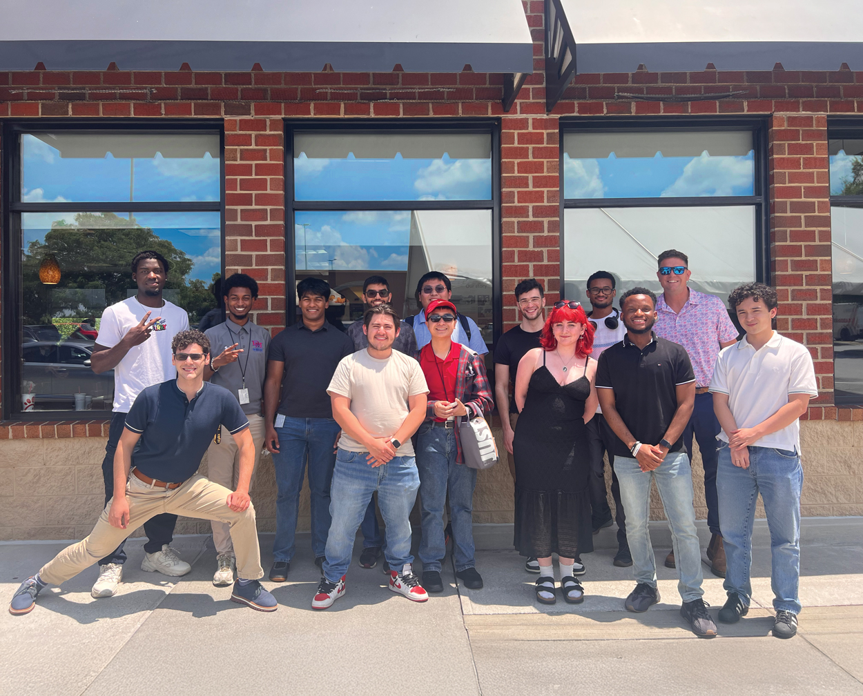 A group of NASA students pose together outside a brick building on a sunny day, smiling for a group photo.