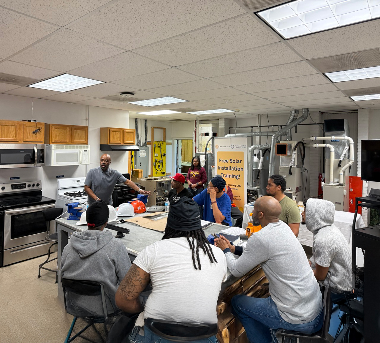 John Deadwyler leads students from TeamBuilders Academy during a hands-on solar installation training session in a lab classroom equipped with tools and technical equipment.