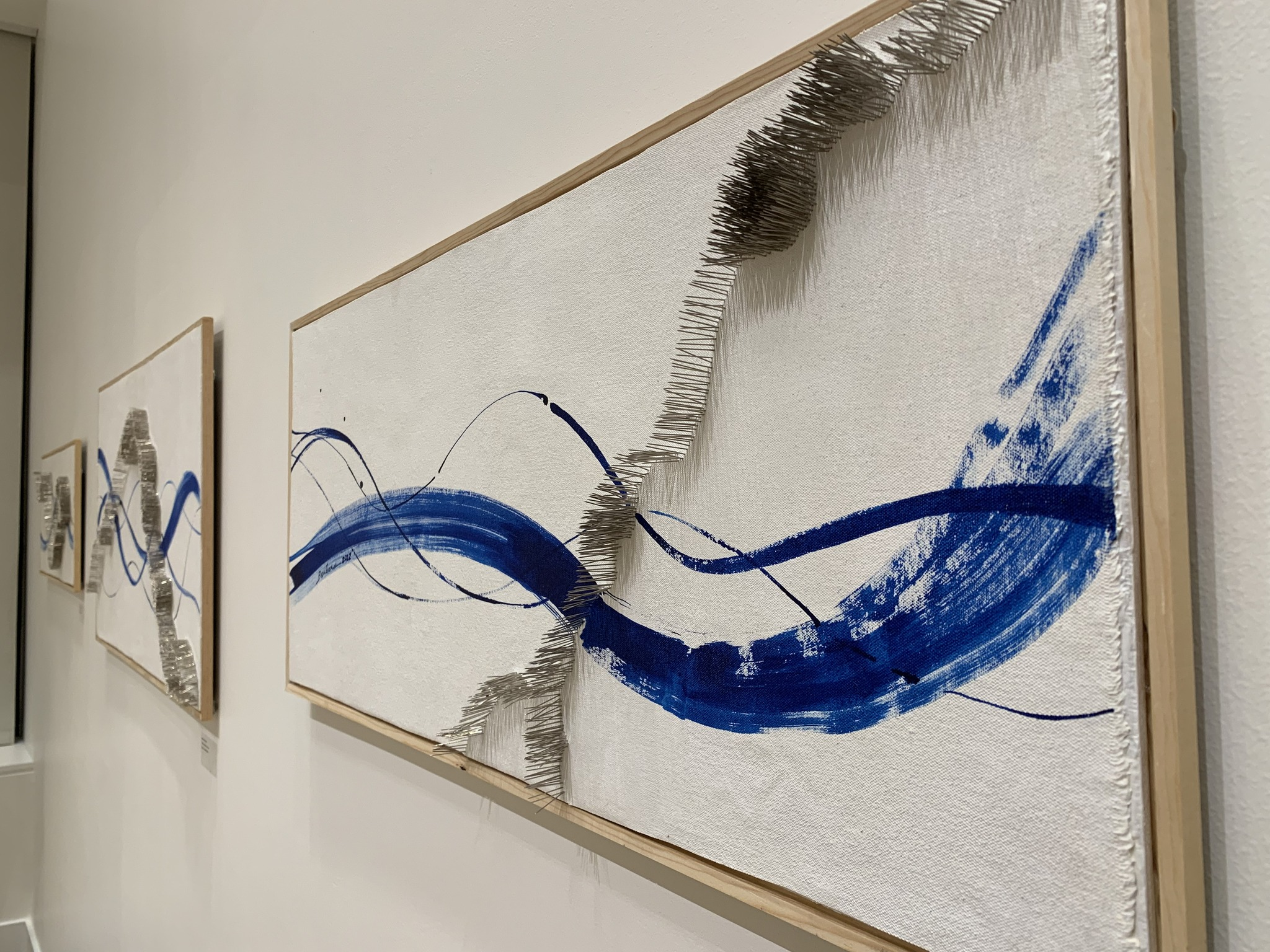 Abstract mixed-media wall art with bold blue brushstrokes and raised metallic nail details on white canvas.