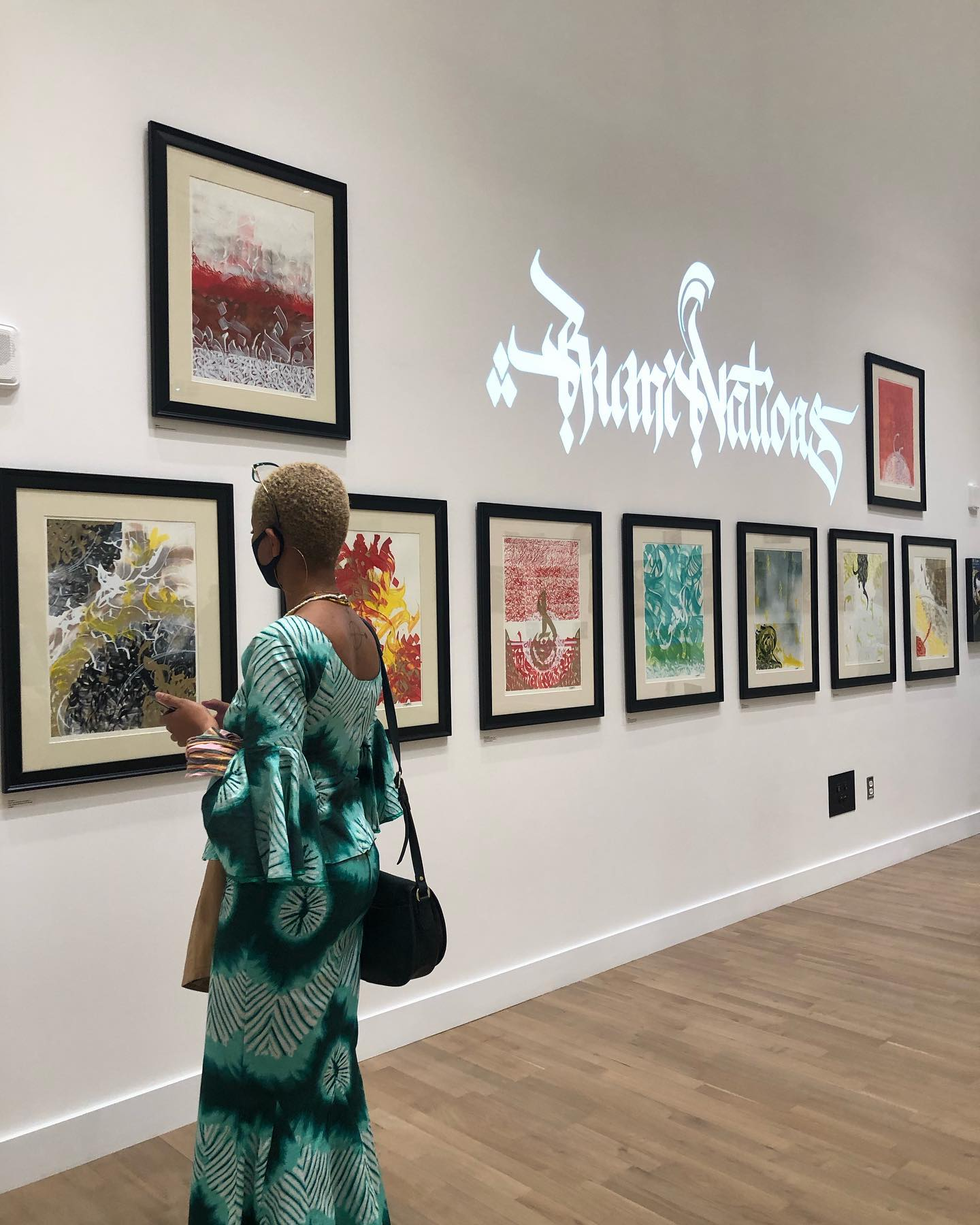 Visitor viewing framed artworks in a gallery with stylized projected text on the wall.