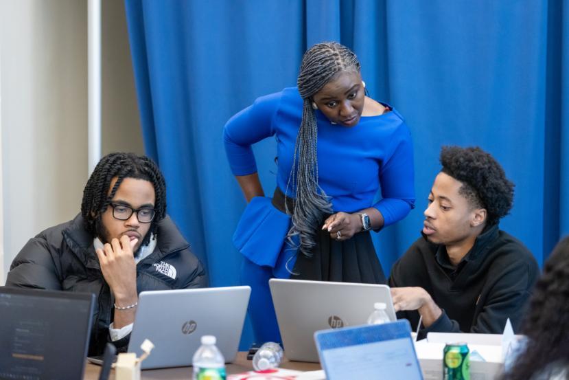 Instructor assisting two students working on laptops during a cybersecurity training session.