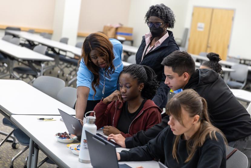 Instructor guiding a group of students working together on laptops during a cybersecurity class.