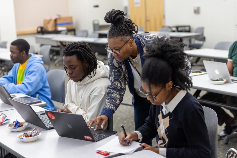 Instructor assisting students working on laptops during a cybersecurity class