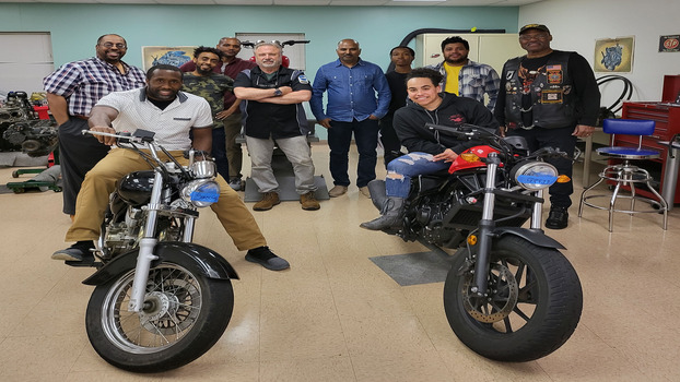 Students and staff together in classroom with two motorcycles