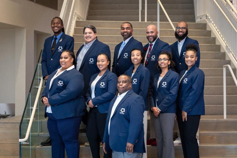 Group photo of COAST advisors in blue blazers standing on a staircase inside a building.