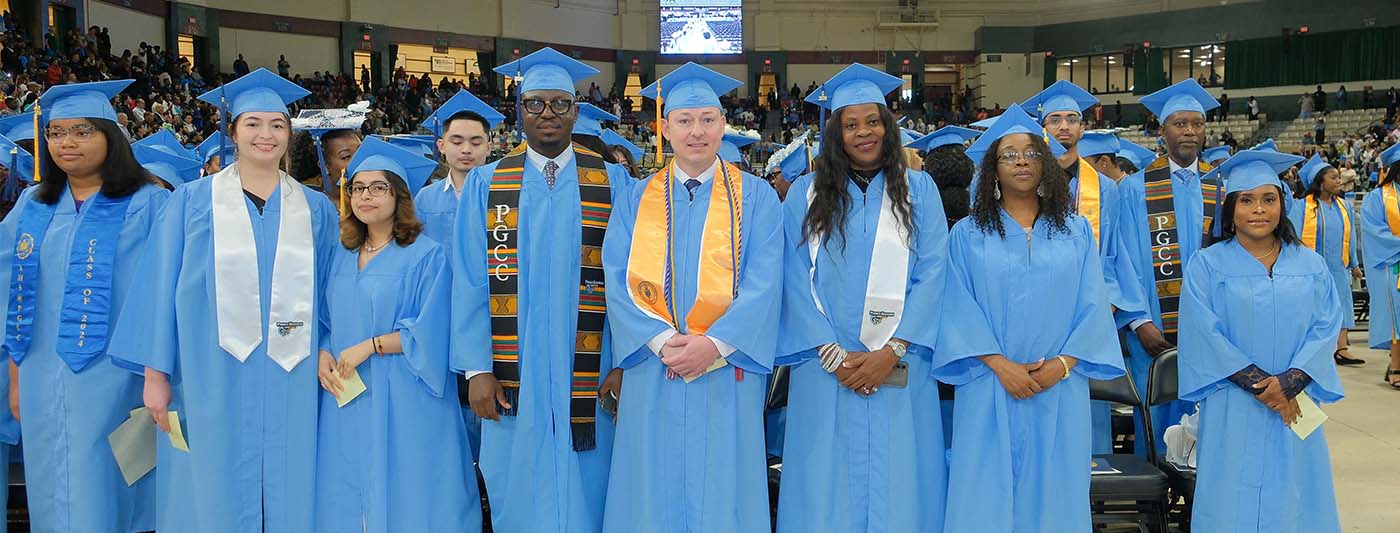 Group of graduates in blue caps and gowns standing together at a commencement